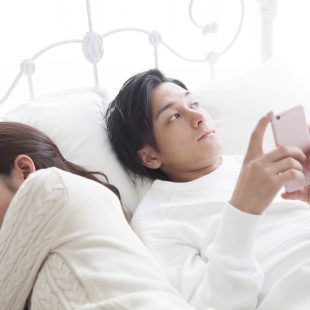 The man is looking at the smartphone in bed